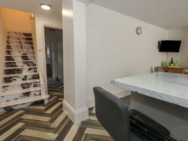 A room with chevron patterned wood flooring stairs with waterfall design a wall clock a wall mounted television and a marble countertop with a black chair at Flat 1 - Sandbanks in Bournemouth
