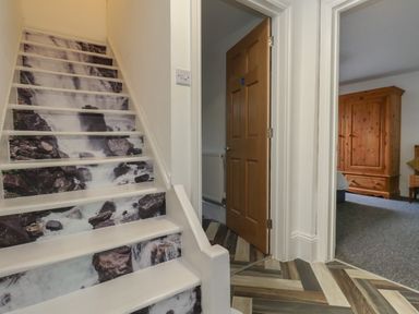 A staircase with waterfall image details on risers next to an open wooden door and a room with wooden furniture at Flat 1 - Sandbanks in Bournemouth