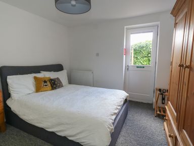 A bedroom with a double bed covered with white bedding two decorative pillows a wooden wardrobe a door leading outside and a gray carpet at Flat 1 - Sandbanks in Bournemouth