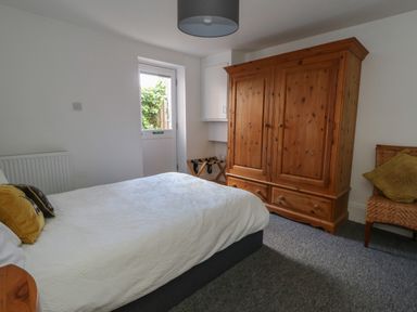 A bedroom with a double bed pillows a wooden wardrobe a wicker chair and a door leading outside at Flat 1 - Sandbanks in Bournemouth