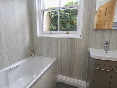 A bathroom with a white bathtub a window showing green leaves a sink with a cabinet and a mirror at Flat 1 - Sandbanks in Bournemouth