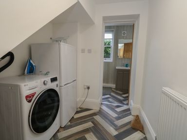 A utility room with a washing machine fridge iron and doorway to a bathroom at Flat 1 - Sandbanks in Bournemouth