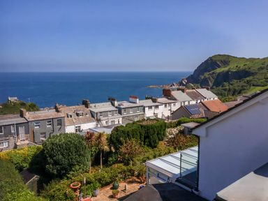 A coastal view with houses and greenery overlooking the sea and cliffs at Combe View in Ilfracombe