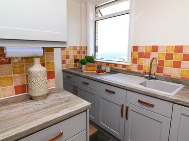 A kitchen with grey cabinets orange and yellow tiled backsplash a sink a vase and bread on the counter at Combe View in Ilfracombe