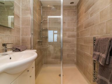 A bathroom with a sink and faucet a walk in shower with glass door and brown tiled walls at Combe View in Ilfracombe