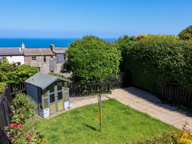 A garden with a small shed a paved walkway a rotary clothesline and hedges at Combe View in Ilfracombe