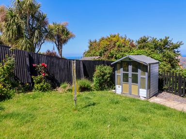 A garden with green grass a small shed a rotary clothesline and trees behind a black wooden fence at Combe View in Ilfracombe