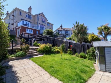 A backyard with grass garden shed stone steps and a large house in the background at Combe View in Ilfracombe