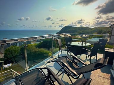 A balcony with deck chairs and table overlooking the ocean at Combe View Ilfracombe
