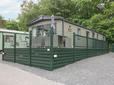 An exterior view of a mobile home with a green fenced deck and outdoor furniture at Mon in Troutbeck Bridge
