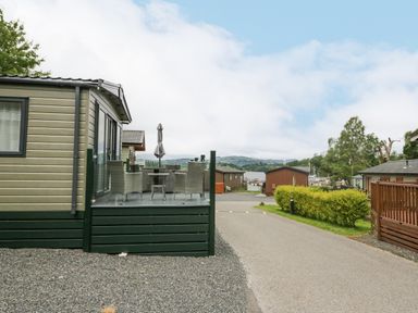 Outdoor seating area with table and chairs next to caravan homes near a road and lake view