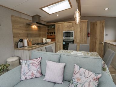 A kitchen and dining area with wooden cabinets a dining table with chairs and a sofa with cushions at Mon in Troutbeck Bridge