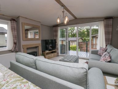 A living room with two gray sofas a gray ottoman a TV on a wooden stand sliding glass doors and plaid curtains at Mon in Troutbeck Bridge