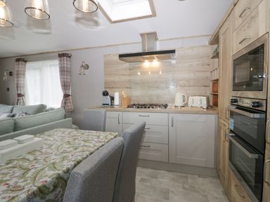 A kitchen with gray cabinets a gas stove a kettle toaster and double oven with a dining table covered with a floral tablecloth and gray chairs at Mon in Troutbeck Bridge