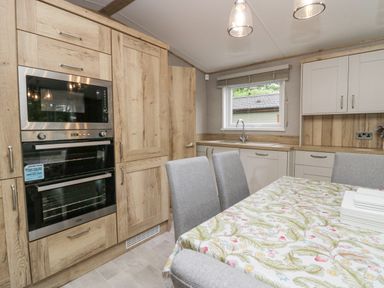 A kitchen with wooden cabinets a built-in oven microwave a window over the sink and a dining table with patterned cloth and gray chairs at Mon Troutbeck Bridge