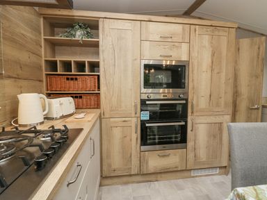 A kitchen with wooden cabinets built-in oven and microwave a kettle toaster and gas stove at Mon in Troutbeck Bridge