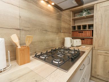 A kitchen countertop with a gas stove kettle toaster wooden utensils paper towel holder and shelves with baskets and a plant at Mon in Troutbeck Bridge