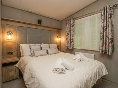 A bedroom with a double bed with pillows and rolled towels and floral curtains at Mon in Troutbeck Bridge