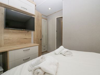 A bedroom with a bed, rolled white towels on the bed, a wall-mounted television, and wooden cabinets at Mon in Troutbeck Bridge