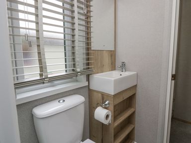 A small bathroom with a toilet next to a wooden sink cabinet with a white sink and a window with blinds