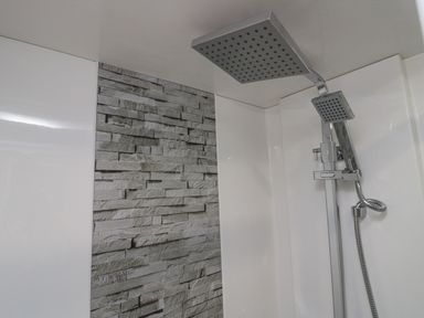A shower area with a dual rain showerhead and a textured stone wall at Mon in Troutbeck Bridge