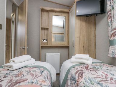 A bedroom with two single beds with floral bedding a mirror a wall-mounted TV and a wooden wardrobe at Mon in Troutbeck Bridge