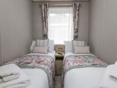 A bedroom with two single beds side by side separated by a wooden nightstand under a window with floral curtains at Mon in Troutbeck Bridge
