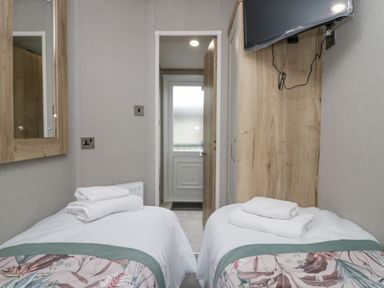 A small bedroom with two single beds two folded towels on each bed a wall-mounted TV and a door at Mon in Troutbeck Bridge