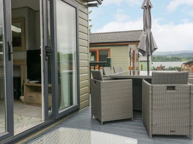 A patio with woven wicker chairs around a glass table and a closed umbrella near a sliding glass door at Mon in Troutbeck Bridge