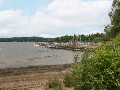 A lake with boats docked at a pier and ducks swimming near the shore at Mon in Troutbeck Bridge
