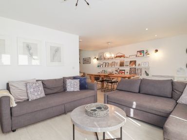 A living room with two gray sofas and a round coffee table with a wicker tray and a dining area with a wooden table and black chairs at Tincroft in Porthtowan