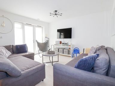 A living room with two gray sofas pillows a wall mounted TV and a round coffee table at Tincroft in Porthtowan
