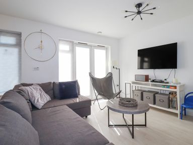 A living room with a grey sofa cushions a butterfly chair a round coffee table a wall clock a flat screen tv and a storage unit at Tincroft in Porthtowan