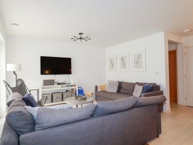 A living room with a wall-mounted television two gray sofas a floor lamp three framed pictures and a white console table at Tincroft in Porthtowan