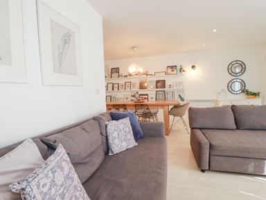 A living room with gray sofas, a wooden dining table with chairs, art on shelves and walls at Tincroft in Porthtowan