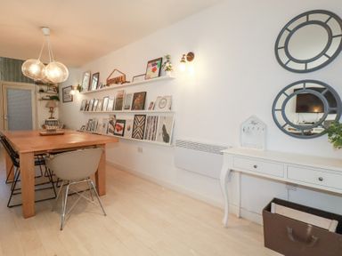 A dining room with a wooden table and chairs artwork on shelves and a white console table with two round mirrors at Tincroft in Porthtowan