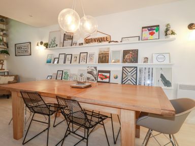 A dining area with a large wooden table black and grey chairs and shelves with framed pictures and signs on the wall at Tincroft in Porthtowan