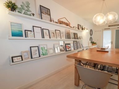 A dining room with a wooden table chairs and framed pictures on shelves on the wall at Tincroft in Porthtowan
