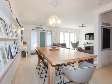 A dining area with a wooden table and chairs next to a living room with sofas and a wall-mounted TV at Tincroft in Porthtowan
