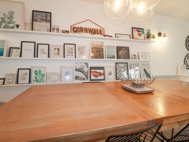 A dining room with a wooden table metal chairs picture frames on shelves and a Cornwall sign at Tincroft in Porthtowan