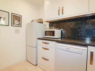 A kitchen corner with a refrigerator a microwave toaster dishwasher and white cabinets at Tincroft in Porthtowan