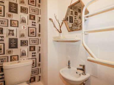 A small bathroom with a toilet sink wall shelf and hexagonal mirror at Tincroft in Porthtowan