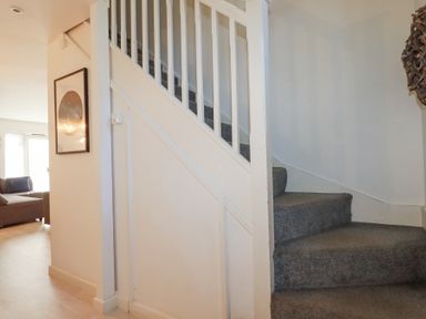 A carpeted staircase next to a wall with framed artwork and a living room with a sofa in the background at Tincroft in Porthtowan