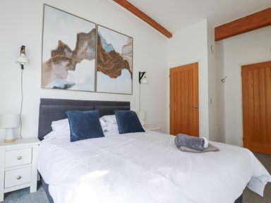 A bedroom with a large bed with blue pillows and white bedding and two wooden doors at Tincroft in Porthtowan