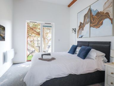 A bedroom with a bed with pillows and towels near glass doors leading to a small balcony with chairs and table at Tincroft in Porthtowan