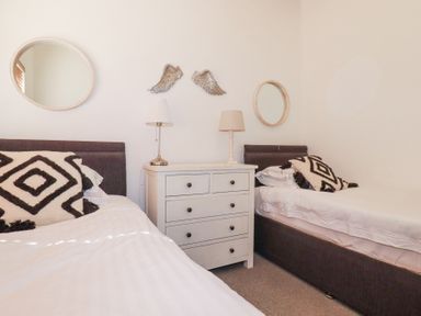 A bedroom with two single beds a white chest of drawers two lamps two round mirrors and wall decorations at Tincroft in Porthtowan