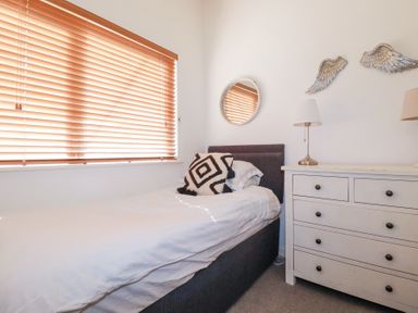 A bedroom with a bed pillow dresser lamps and round mirror at Tincroft in Porthtowan