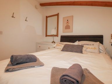 A bedroom with a bed with two rolled towels on it a bedside table with a lamp a wall mirror and a framed picture at Tincroft in Porthtowan