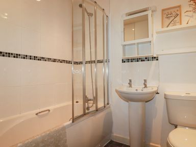 A bathroom with a bathtub and shower, a pedestal sink, a toilet, a mirrored cabinet, and a shelf with a framed sign at Tincroft in Porthtowan