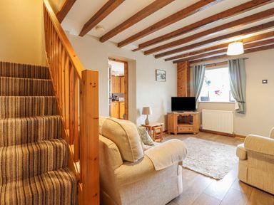 A living room with beige sofas a wooden staircase a television on a wooden cabinet and a window with curtains at Llys-y-Wennol in Penmachno